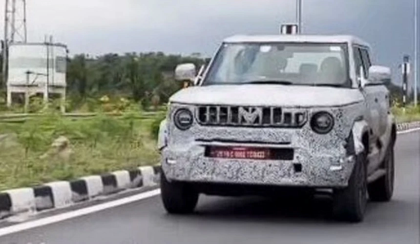 Front and side view of 2025 Mahindra Bolero spied testing camouflaged on Indian roads, showcasing new grille, bumper, and body cladding